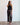 Woman wearing a black halter top and patterned pants against a white wall.