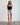 Woman wearing a black strapless top and denim shorts against a white wall.